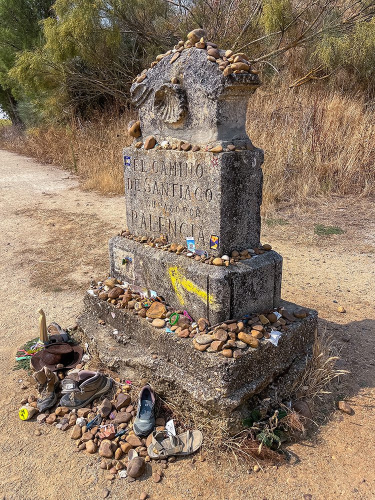 Camino de Santiago monument covered with stones and pilgrim mementos beside the trail to Sahagún