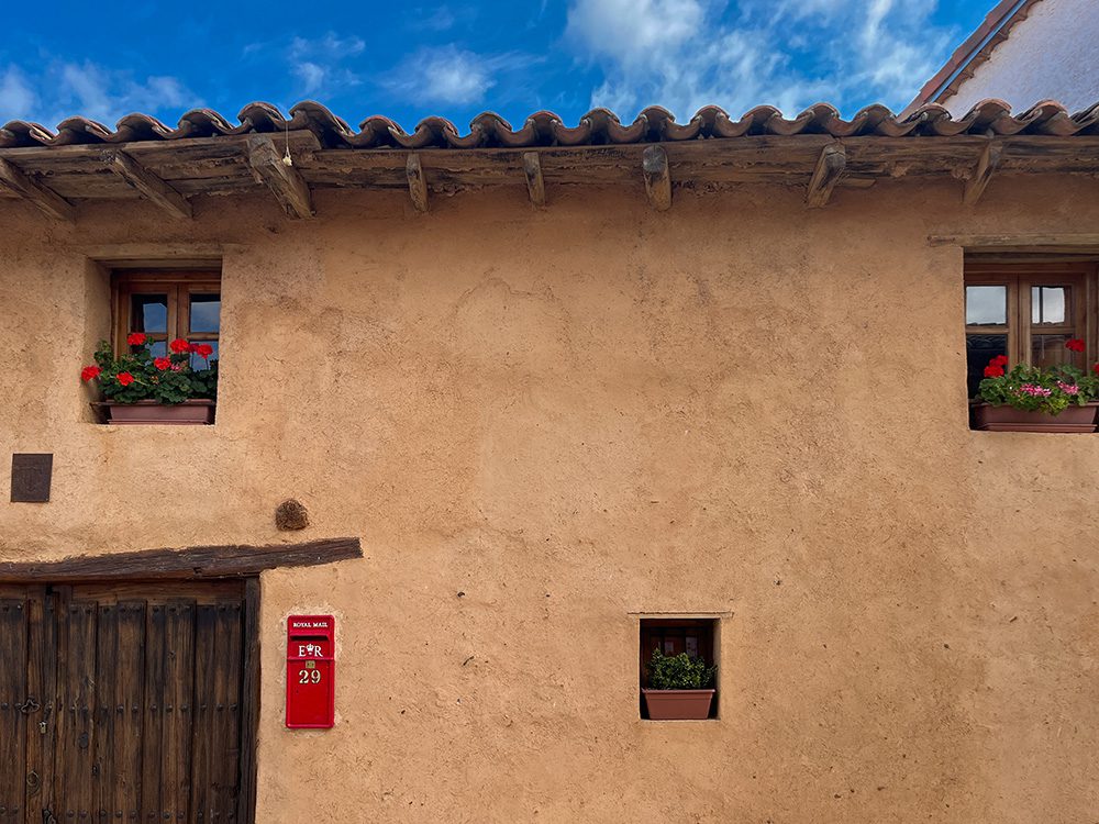 Traditional adobe house with red Royal Mail post box and geraniums in Reliegos