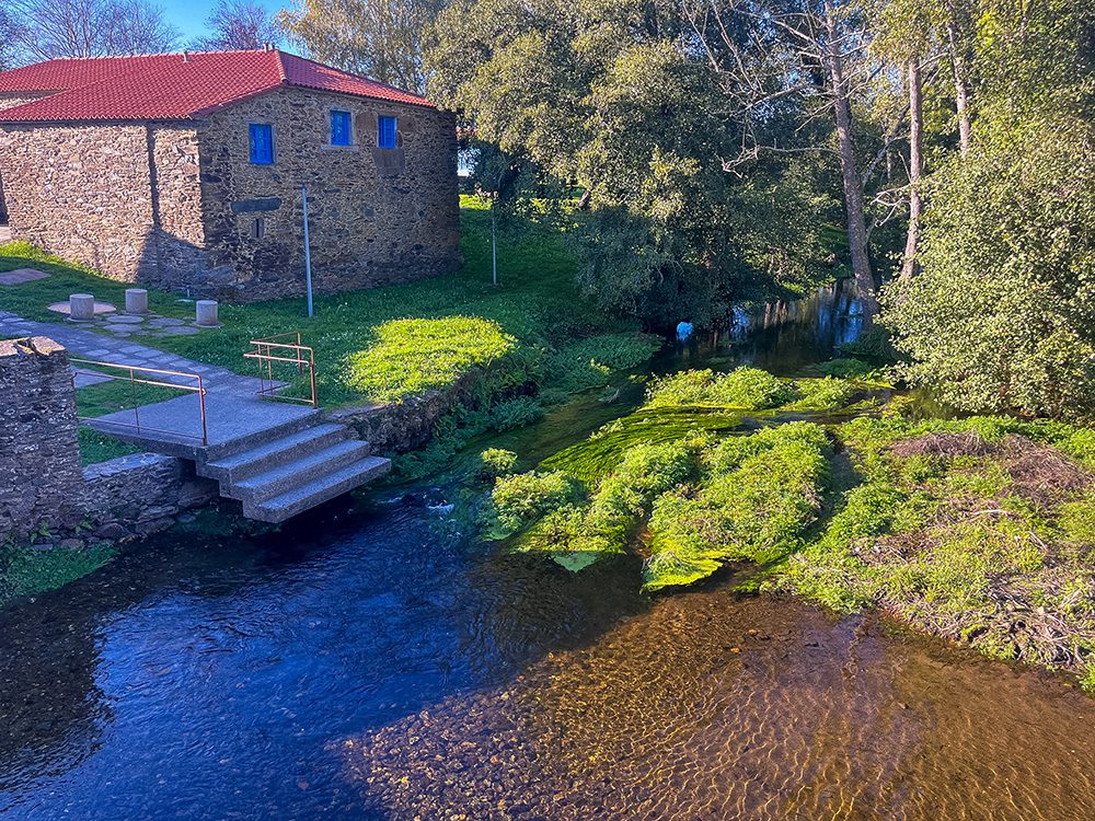 Clear river flowing past traditional stone buildings at Ribadiso de Baixo on the Camino Francés