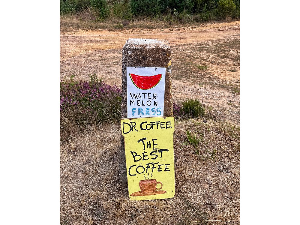 Hand-painted Dr Coffee sign offering coffee, water and melon beside the Camino Francés